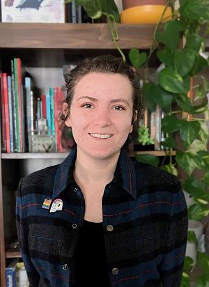 Photo of Tristan smiling and standing in front of a bookshelf