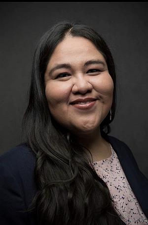 portrait of a Native American woman with long black hair wearing a pink shirt and black blazer while smiling on a dark gray background